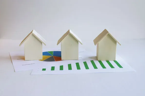 Three wooden model houses resting on a green bar chart and pie chart, symbolising domestic energy efficiency data and property performance.