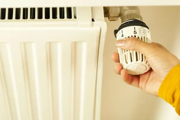 A hand adjusting a thermostatic radiator valve to manage room temperature and improve domestic energy efficiency