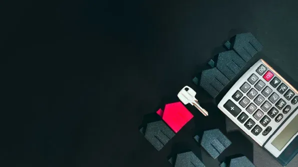 A picture of small model houses, a key and a calculator on a dark background representing property costs