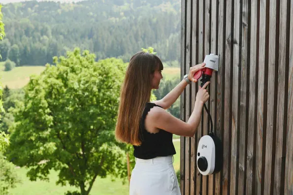 A woman connecting a portable electric vehicle charger to an outdoor wall socket at a residential property