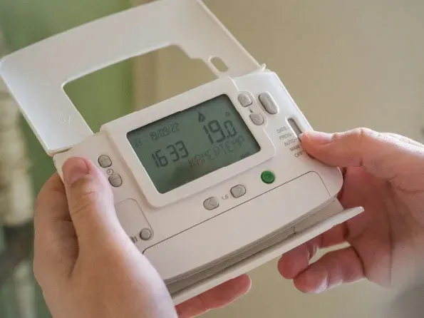 A close-up of hands adjusting a white digital heating thermostat.